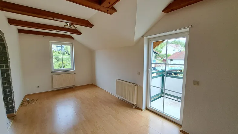 Helles Zimmer mit Holzbalken, Parkettboden und Zugang zu einem französischen Balkon.