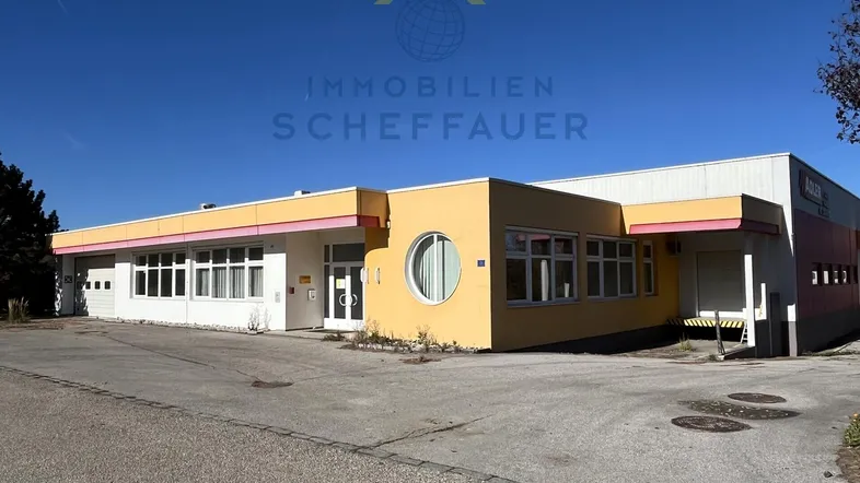 Gebäudeansicht eines Gewerbeobjekts mit gelber Fassade und großem Parkplatz unter blauem Himmel.