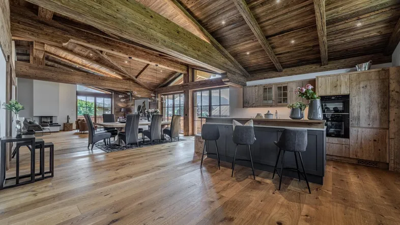 Geräumiger offener Wohn- und Essbereich mit Holzbalkendecke, Eichenparkett und integrierter Küche im Chalet-Stil.