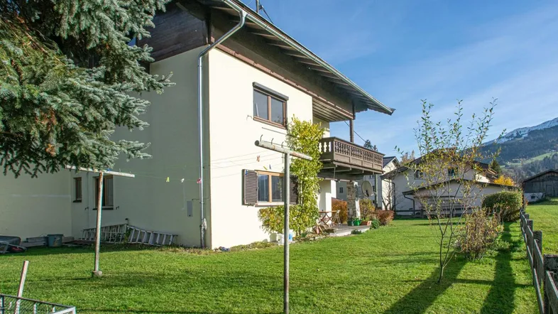 Seitenansicht des traditionellen Hauses mit gepflegtem Rasen und Balkon, umgeben von Bäumen.