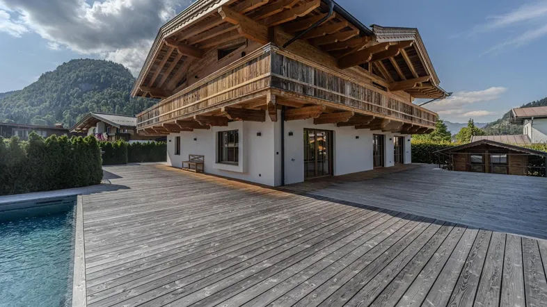 Modernes Chalet mit Holzfassade, großem Pool und Holzterrasse im Grünen mit Bergblick.