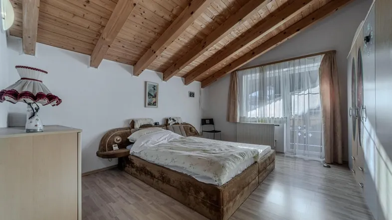 Gemütliches Schlafzimmer im Dachgeschoss mit Holzbalkendecke, Laminatboden und großem Fenster.