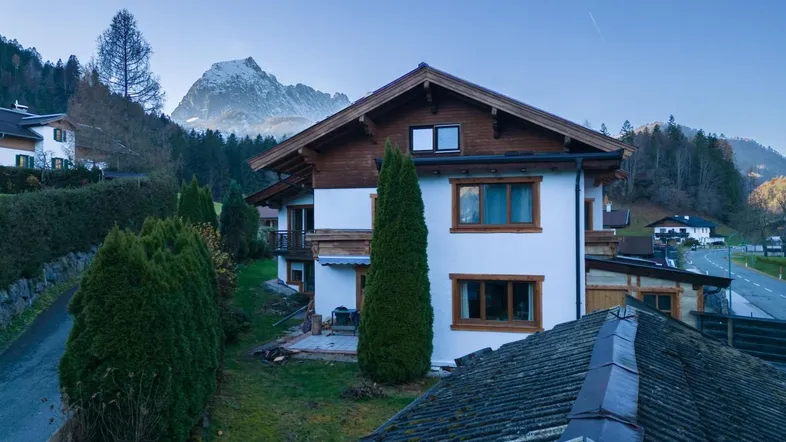 Traditionelles Chalet mit weißer Fassade, Holzelementen und beeindruckendem Bergblick in grüner Umgebung.