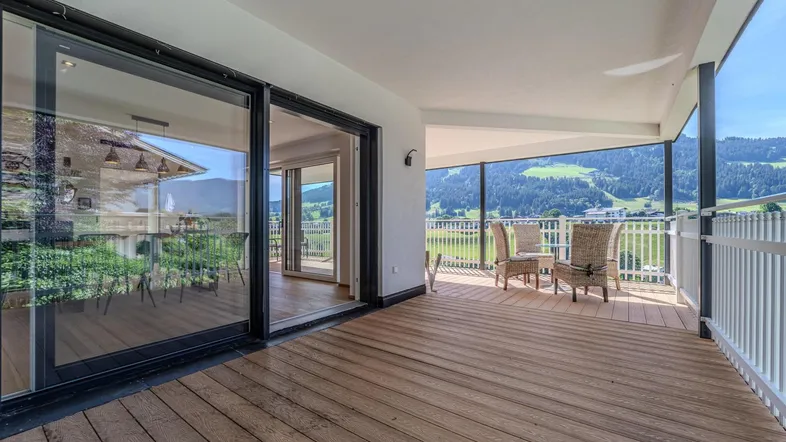 Geräumige Terrasse mit Holzboden, Sitzgelegenheiten und weitem Blick auf die umliegende Berglandschaft.