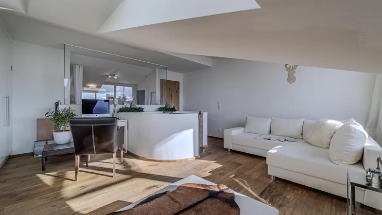 Helles Wohnzimmer im Dachgeschoss mit Holzboden, weißem Sofa und integriertem Arbeitsbereich.