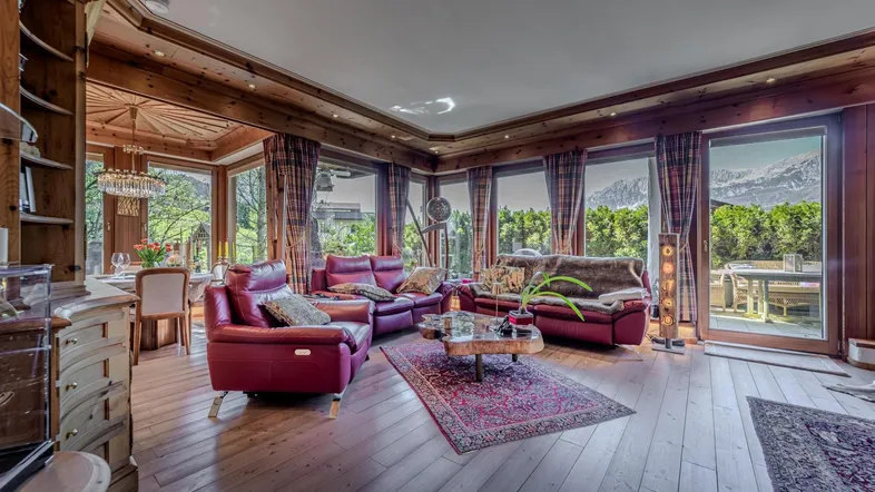 Helles Wohn- und Esszimmer im alpinen Stil mit Holzböden, roten Ledersofas und Bergblick durch große Fenster.