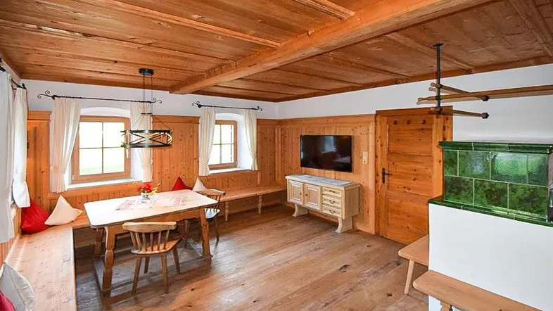 Gemütlicher Wohn- und Essbereich im alpinen Stil mit Holzbalkendecke und traditionellem Kachelofen.