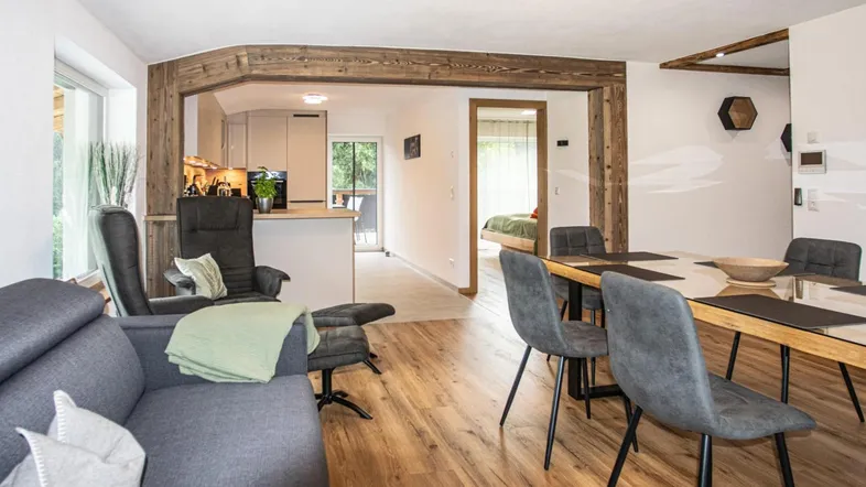Heller offener Wohn- und Essbereich mit Holzbalken, Parkettboden und Zugang zur Küche.
