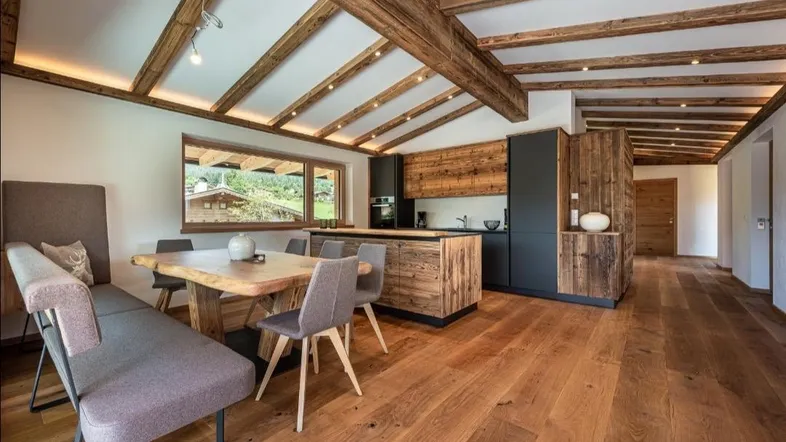 Geräumige offene Küche mit Holzbalkendecke, moderner Ausstattung und großem Esstisch mit Bergblick.