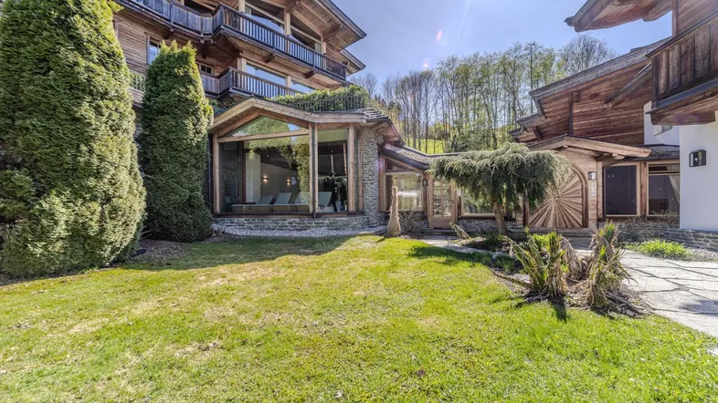 Großes Holzchalet mit traditioneller Architektur, umgeben von einem gepflegten Rasen und Bäumen.