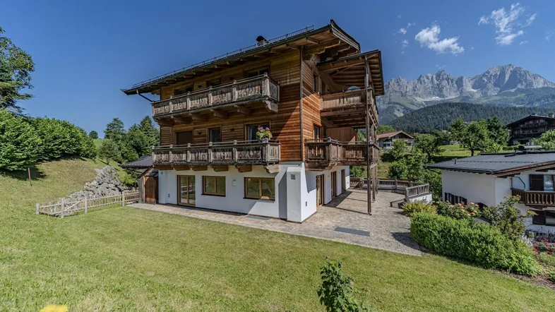 Großes Holzchalet mit traditioneller Architektur, mehreren Balkonen, weitläufigem Garten und beeindruckendem Bergblick.