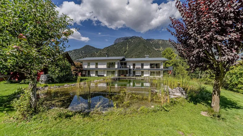 Modernes Gebäude mit großem Naturteich und Bergblick in grüner Umgebung.