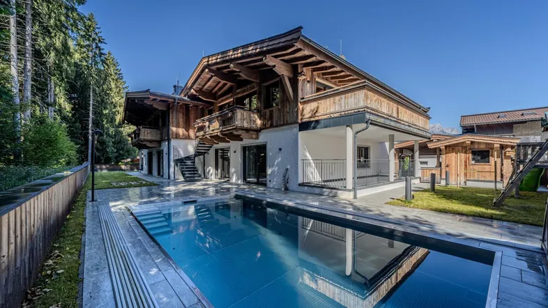 Luxuriöses Chalet mit großem Außenpool und weitläufiger Terrasse, umgeben von grünen Bäumen.