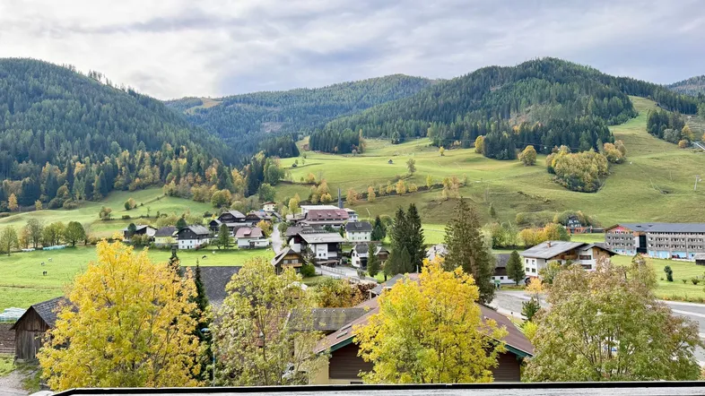 Panoramablick vom Balkon auf eine malerische Berglandschaft mit herbstlichen Bäumen und einem charmanten Dorf.