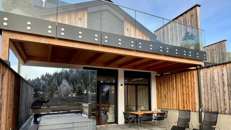 Moderne Terrasse mit Whirlpool, Essbereich und Balkon, umgeben von einer verschneiten Berglandschaft.