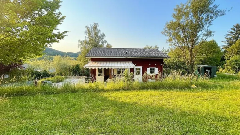 Rotes Holzhaus mit weißer Markise und weitläufiger Rasenfläche im Vordergrund.