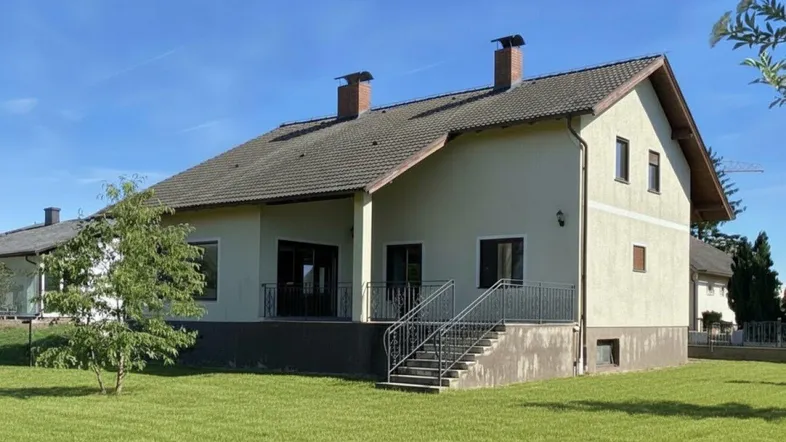 Rückansicht des Hauses mit überdachter Terrasse und Treppenzugang zum weitläufigen Garten.