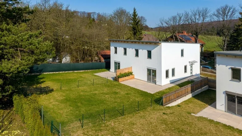 Luftaufnahme eines modernen Einfamilienhauses mit großem Garten und Terrasse in ländlicher Umgebung.