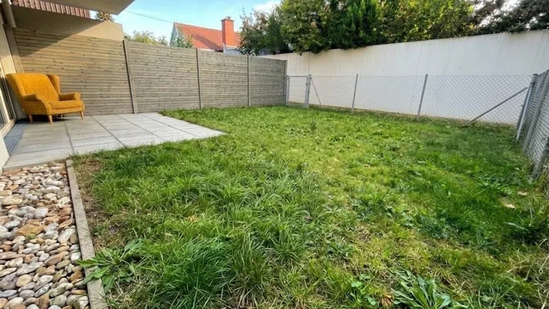 Gepflasterte Terrasse mit Gartenbereich und einem Sessel, umgeben von einem Holzzaun.