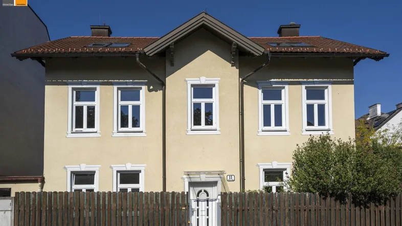 Vorderansicht eines charmanten Einfamilienhauses mit gelber Fassade und Holzzaun.