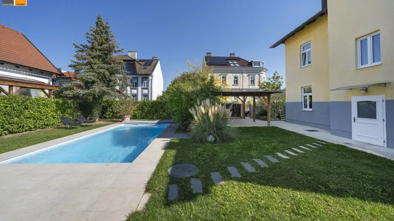 Großer Garten mit Swimmingpool, Liegewiese und gepflegten Pflanzen unter blauem Himmel.