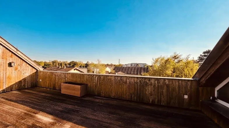 Geräumige Dachterrasse mit Holzboden und weitem Blick über die Nachbarschaft unter blauem Himmel.