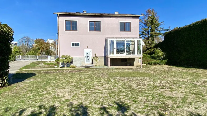 Rosa gestrichenes Haus mit Wintergarten und großem Rasenbereich unter blauem Himmel.