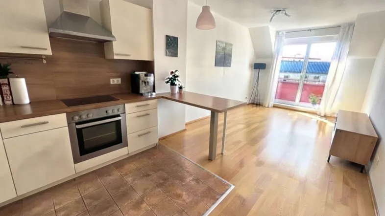 Offener Wohn-Essbereich mit integrierter Küche, Holzboden und Zugang zum Balkon.