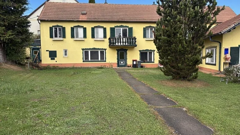 Gelbes Haus mit grünen Fensterläden und einem kleinen Balkon, umgeben von Rasen.