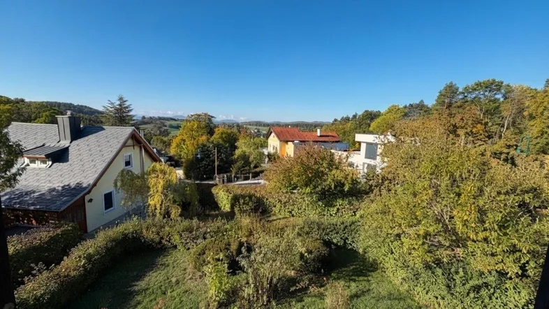 Weitläufiger Blick über die grüne Landschaft mit umliegenden Häusern unter blauem Himmel.