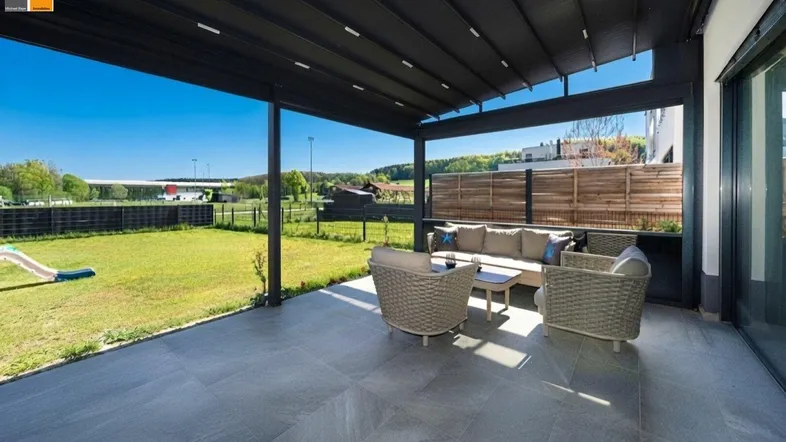 Geräumige Terrasse mit modernen Fliesen, bequemen Gartenmöbeln und Blick auf den grünen Garten.