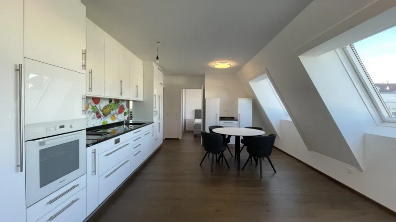 Moderne Küche mit weißen Hochglanzfronten, integrierten Geräten und Essbereich unter Dachschrägen.