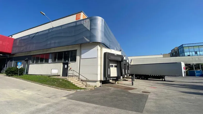 Außenansicht eines Industriegebäudes mit Laderampen und einem geparkten LKW-Anhänger unter blauem Himmel.