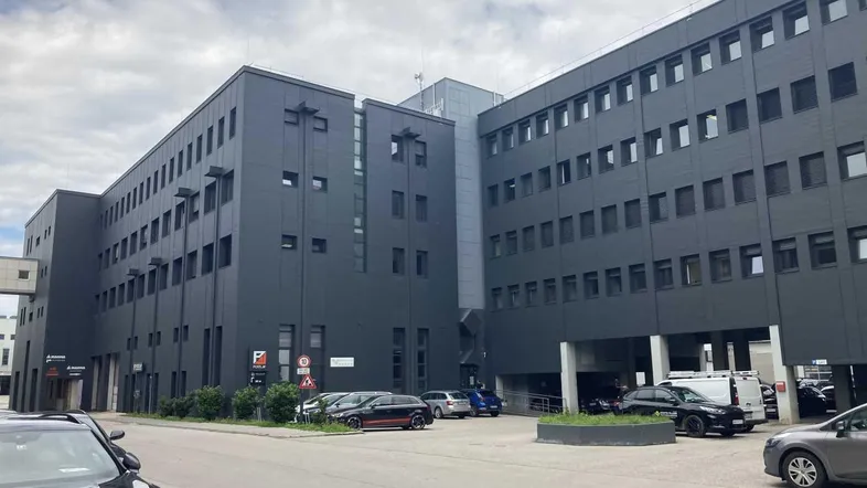 Modernes Geschäftsgebäude mit dunkler Fassade und Parkplätzen davor unter bewölktem Himmel.