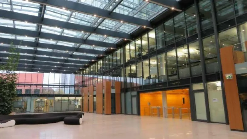 Großzügige, lichtdurchflutete Lobby mit Glasdach, modernen Sitzgelegenheiten und Zugang zu Büroräumen.
