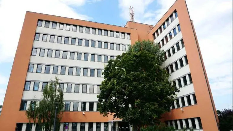 Großes Bürogebäude mit moderner Architektur, vielen Fenstern und orangefarbener Fassade unter bewölktem Himmel.