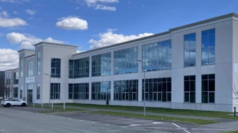 Modernes Bürogebäude mit großer Glasfassade und einem Parkplatz unter blauem Himmel.