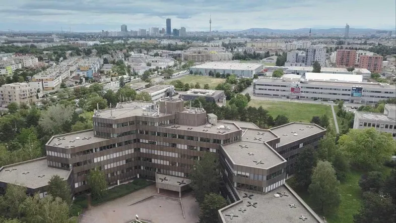 Luftaufnahme eines großen Bürogebäudes mit komplexer Architektur und Blick auf die Stadtlandschaft im Hintergrund.