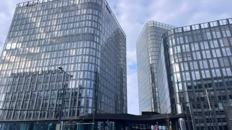 Modernes Bürogebäude mit Glasfassade und geschwungenen Formen unter bewölktem Himmel.