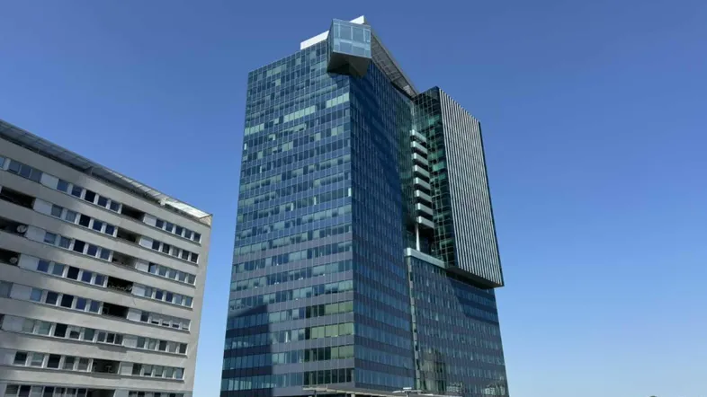 Modernes Hochhaus mit Glasfassade und klarem Himmel, umgeben von städtischer Architektur.