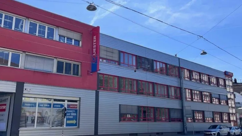 Modernes Geschäftsgebäude mit roter und grauer Fassade sowie großen Fenstern an einer Straße gelegen.
