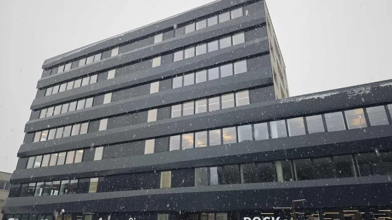 Modernes Geschäftsgebäude mit dunkler Fassade und großen Fenstern, im Winter bei Schneefall.