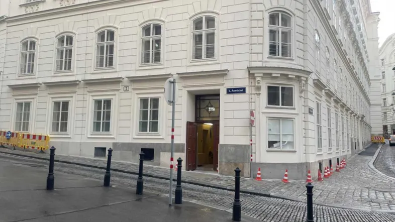 Historisches Eckgebäude mit weißer Fassade und großen Fenstern an einer gepflasterten Straße.