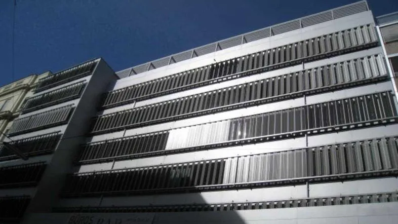 Moderne Fassade eines Bürogebäudes mit zahlreichen horizontalen Lamellen und einem klaren blauen Himmel.