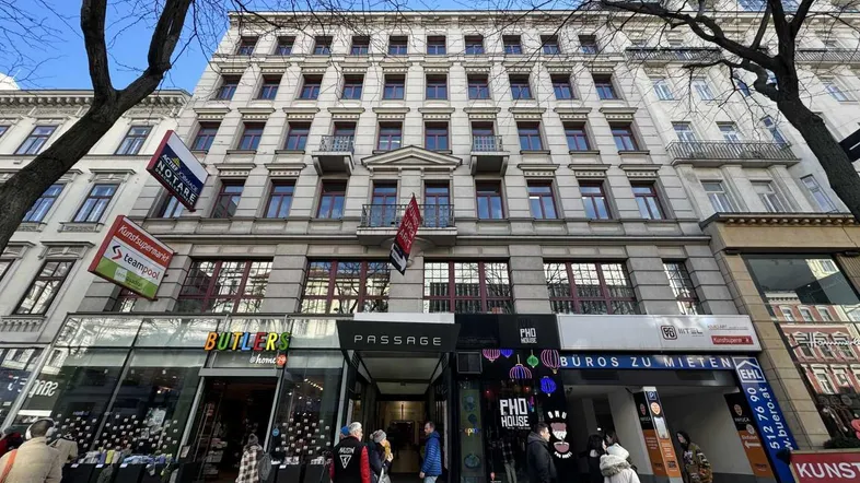 Historisches Gebäude mit klassischer Fassade und Geschäften im Erdgeschoss, belebt durch Passanten.