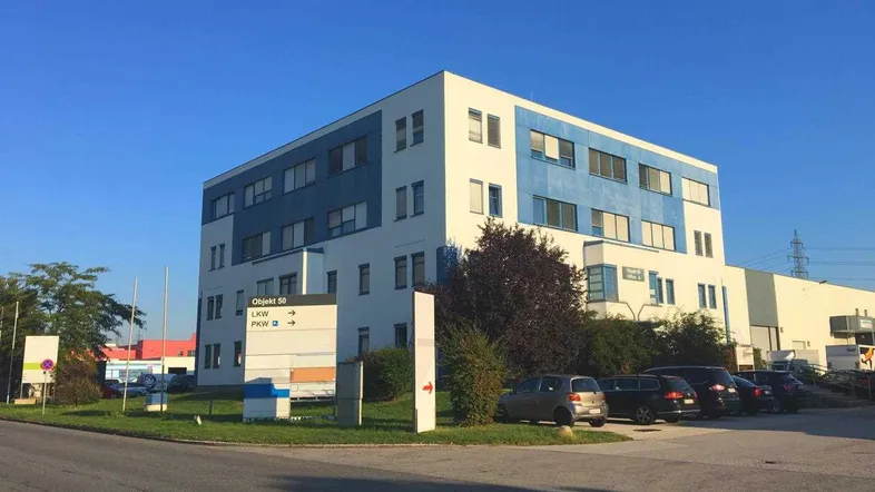 Modernes Bürogebäude mit blauer und weißer Fassade sowie Parkplätzen im Vordergrund unter klarem Himmel.