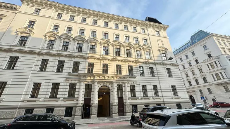 Klassisches Gebäude mit eleganter Fassade und vielen Fenstern, umgeben von parkenden Autos auf der Straße.