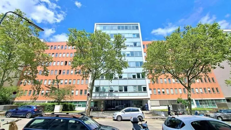 Außenansicht eines modernen Bürogebäudes mit Glasfassade und Bäumen davor unter blauem Himmel.