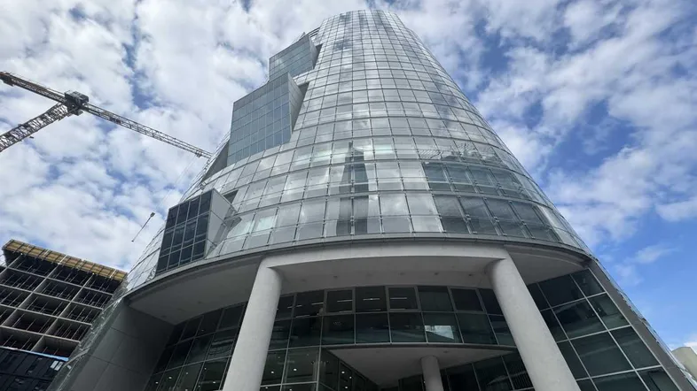 Modernes Hochhaus mit geschwungener Glasfassade unter bewölktem Himmel, umgeben von Baustellenaktivitäten.
