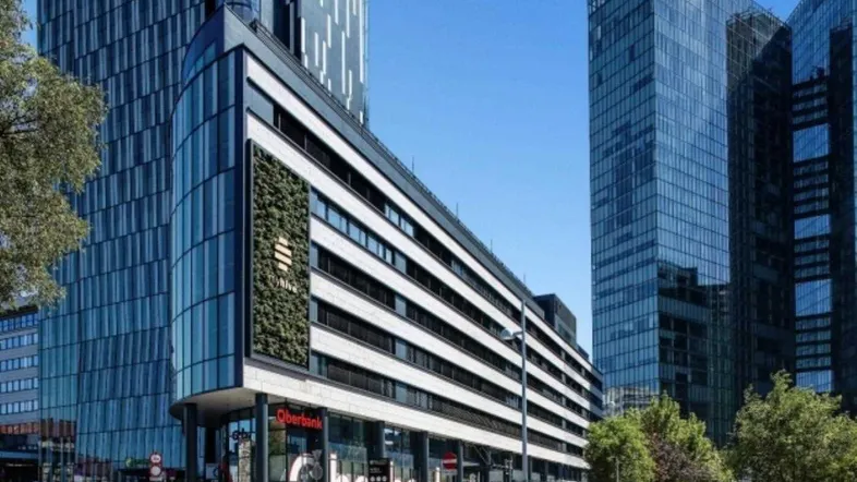 Modernes Bürogebäude mit Glasfassade und vertikaler Begrünung in urbaner Umgebung unter blauem Himmel.